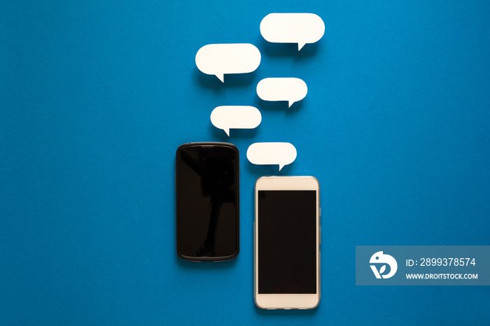 Smartphones with paper speech bubbles on blue background. Communication concept. Top view. Copy spac