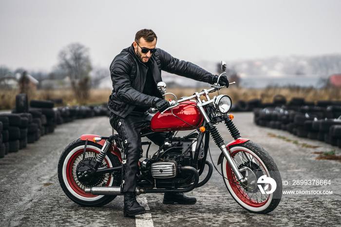 Red motorbike with rider. A man in a black leather jacket and pants stands sideways in the middle of