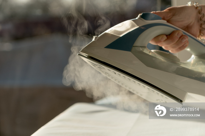 Flatten laundry on an ironing board with a steam iron. Concept: housework