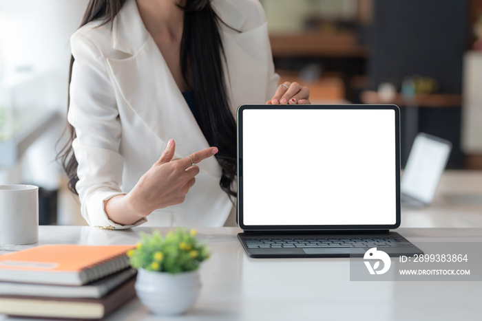 Close-up of a businesswoman hand pointing at a tablet a blank white screen at the office. Mock up.