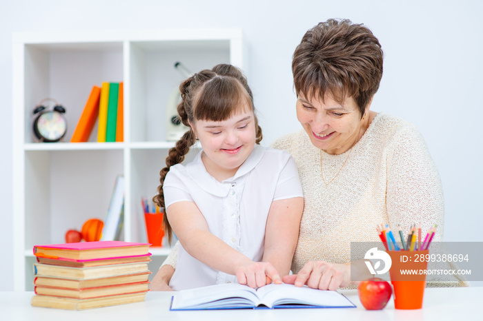 A girl with down syndrome and her mother are sitting at home at a table with an open book in front o