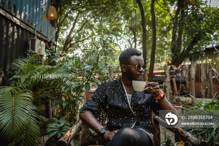 a black man holding in tea cup in a garden