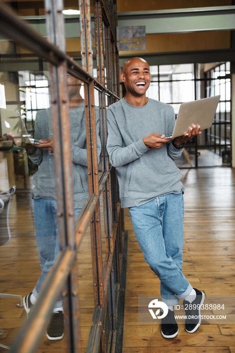 Image of bald african american man holding laptop while working in office