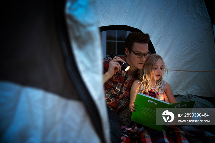 Father and daughter reading book in tent