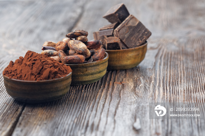 Dark chocolate pieces, cocoa powder and cocoa beans on a wooden table