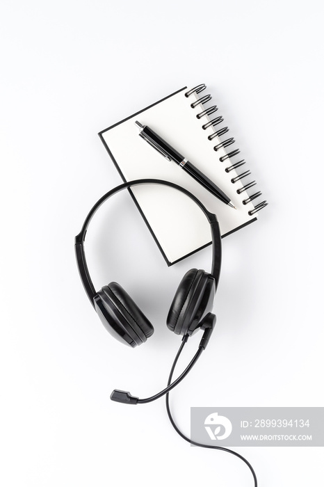 白色桌面上带笔记本和笔的服务台耳机。呼叫中心概念。俯视图