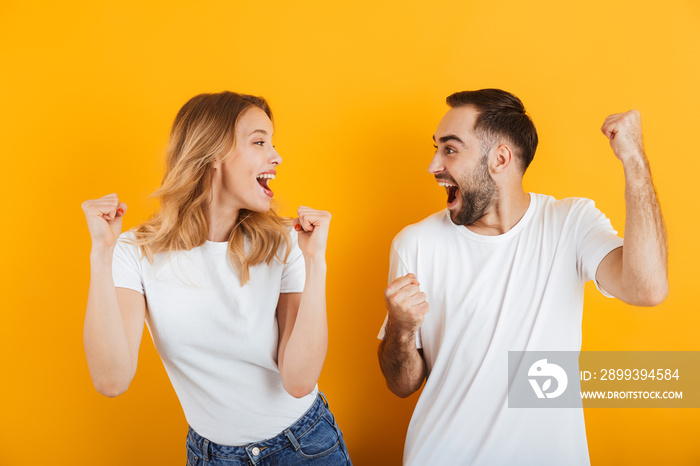 Portrait of positive pleased couple man and woman in basic t-shirts rejoicing and clenching fists