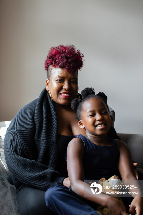 African American mother and daughter sitting on couch smiling together