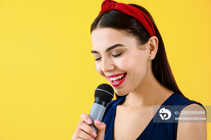 Beautiful young female singer with microphone on color background