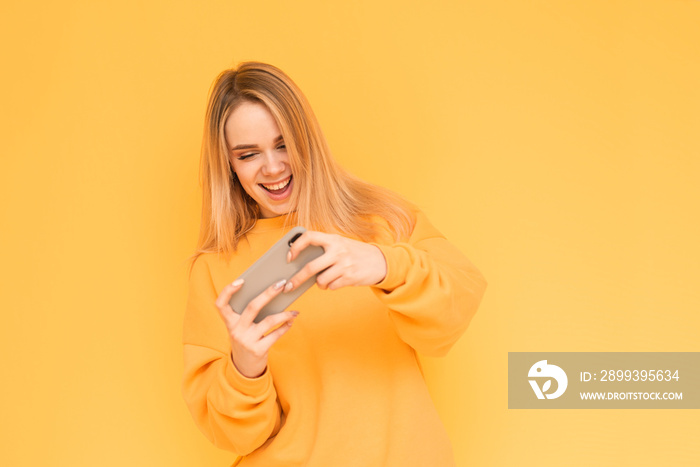 Portrait of a teenage girl in orange clothes playing mobile games on a smartphone, smiling, looking 