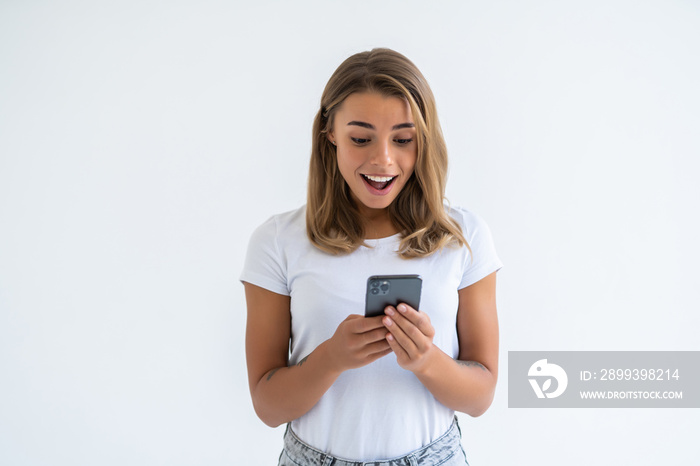 Portrait of a surprised attractive girl holding mobile phone and looking at camera isolated over whi