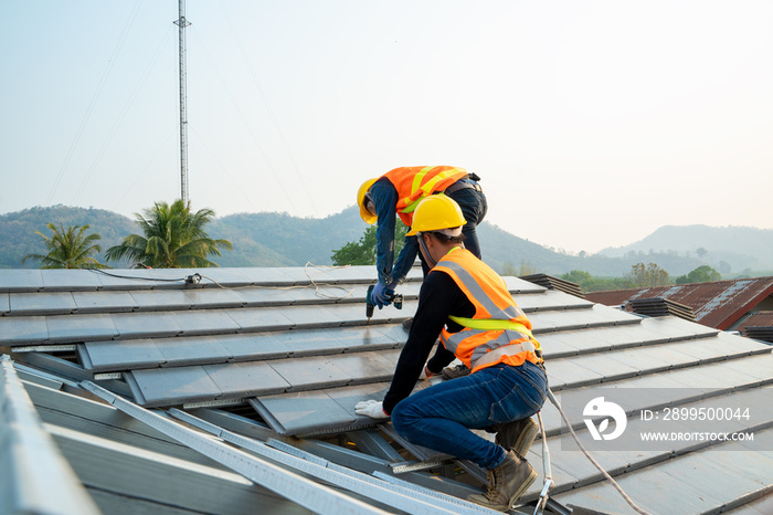 Roofer worker in special protective workwear and gloves installing new roof under construction residential building.