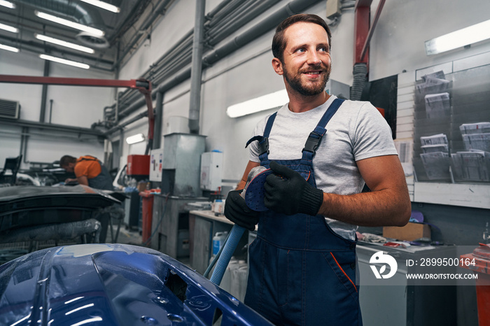 Male car workshop worker taking care of sander after work