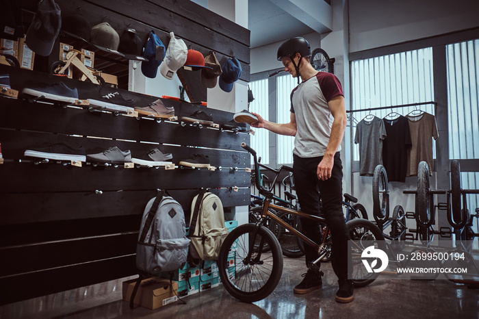 Teenage BMX rider standing with his bike, choosing new sneakers in a shop.