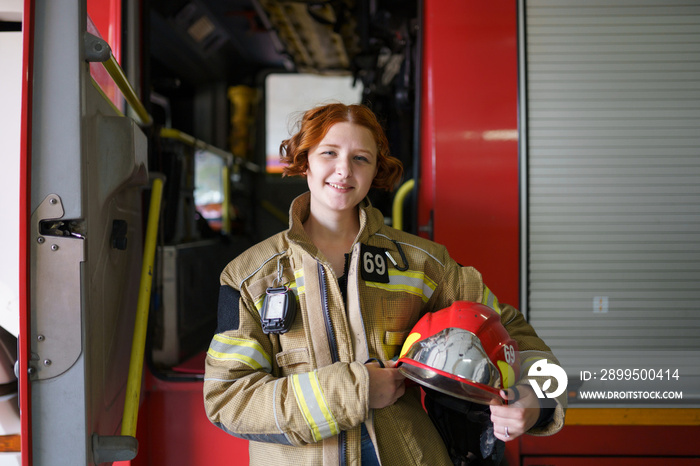 Photo of woman firefighter with helmet in hands against backdrop of fire truck