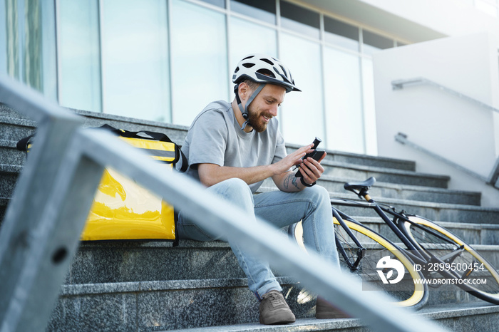 Express food delivery courier sitting on the stairs with insulated bag and bicycle.