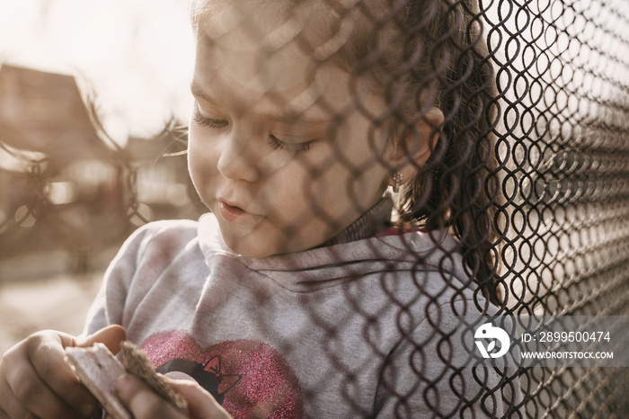 A little girl with a sad look behind a metal fence. Social problem of refugees and forced migrants