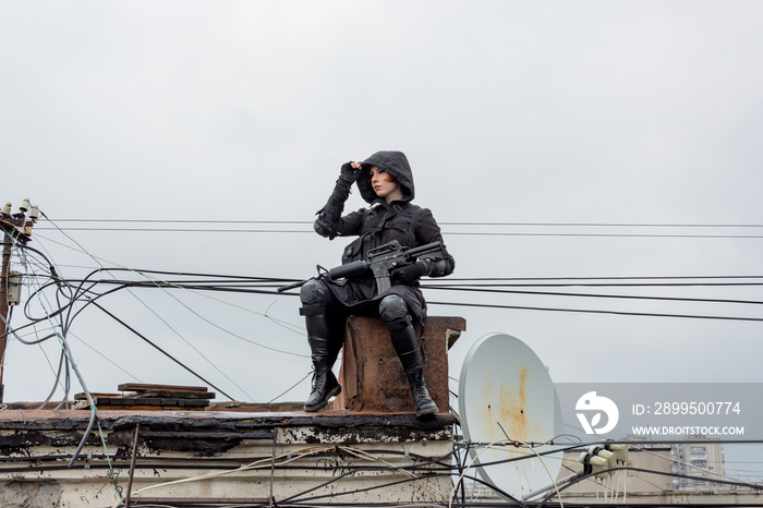 Young woman in modern black techwear style with rifle posing on the rooftop, portrait of redhead woman cyperpunk or   post apocalyptic concept