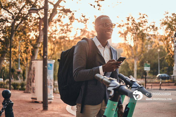 Attractive american tourist in sunglasses is paying for electrical scooter using his mobile phone.