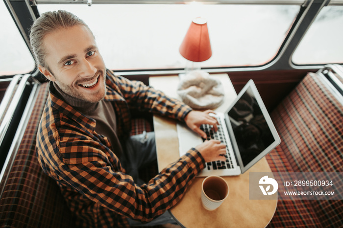 Young hipster male sitting with laptop in bus cafe