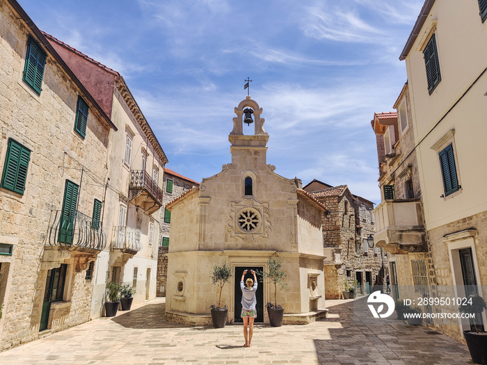 Female tourist taking photo of mall church on square of small urban village of Stari grad on Hvar island in Croatia, Adriatic Sea, Europe.