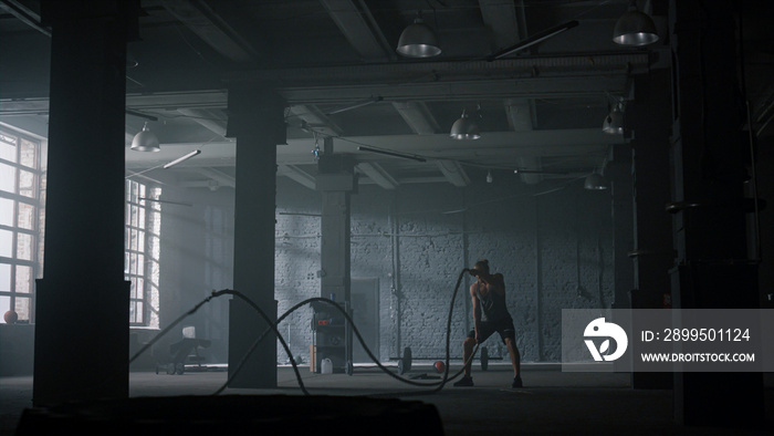 Guy battling ropes in gym. Athletic man doing crossfit workout in loft building