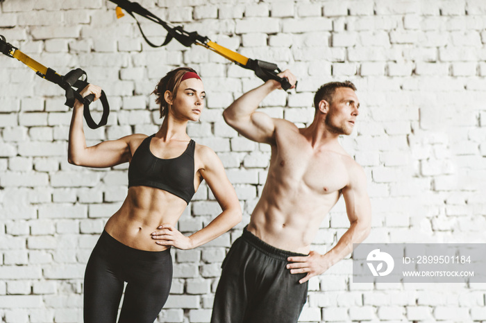 Athletic man and woman doing TRX workout at gym.