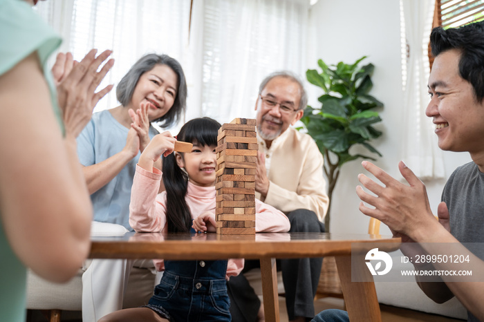 Asian big family cheering kid playing Jenga game in the living room.