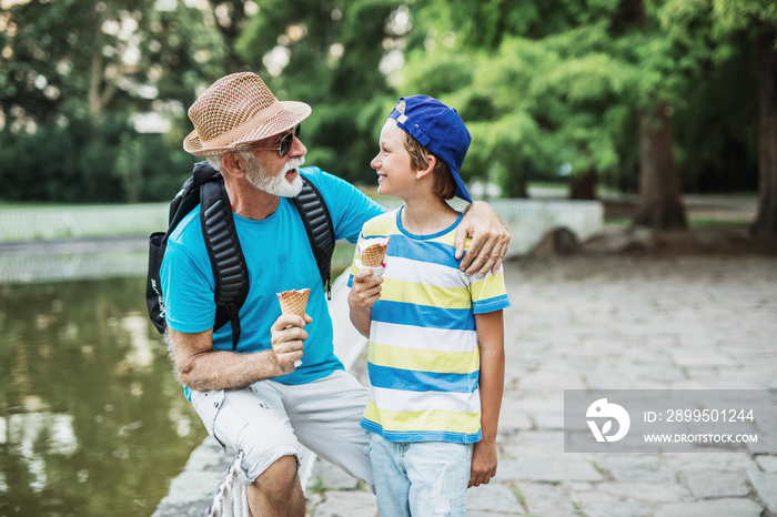 Happy grandfather enjoying with his grandson while eating ice cream outdoors in park.