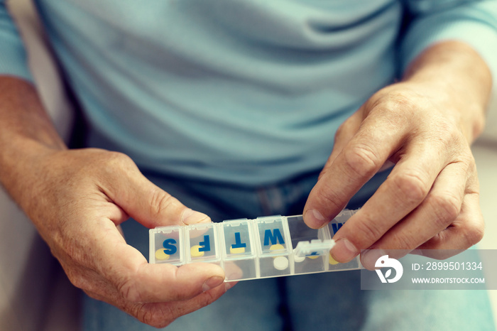 This is really helpful. Close up of an elderly man sitting on a sofa and opening a weekly organizer while taking his pills.