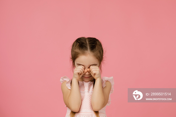 upset little child girl is crying on pink background. girl wiping tears