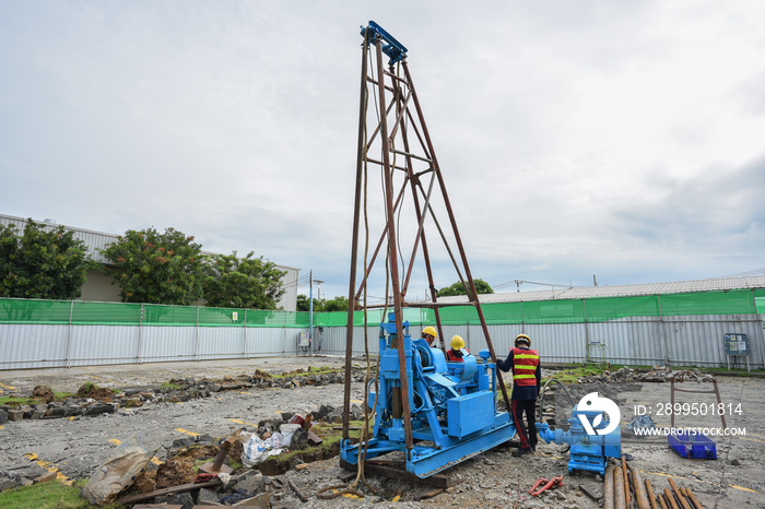 Construction workers assembly rig and machine for soil investigation works at construction site.