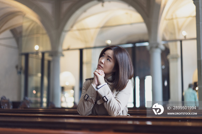 A Christian girl is sitting and praying with broken heart in the church.