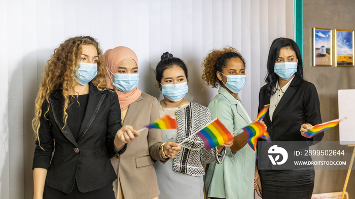 Five business women from different ethnic races and cultures with protective mask express support for LGBT with flags in an office