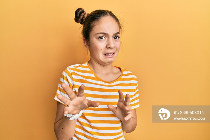 Beautiful brunette little girl wearing casual striped t shirt disgusted expression, displeased and fearful doing disgust face because aversion reaction.