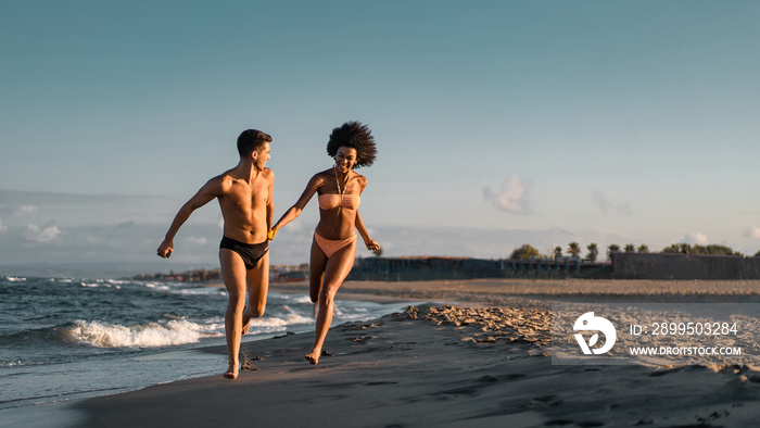 Joyful interracial couple running on the beach. Mixed race young lovers having fun on vacation concept