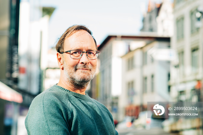 Outdoor portrait of 50 - 55 year old man wearing green pullover and eyeglasses