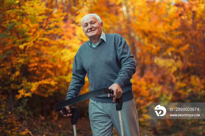 Happy senior man with a walking disability enjoying a walk in an autumn park pushing her walker or wheel chair.