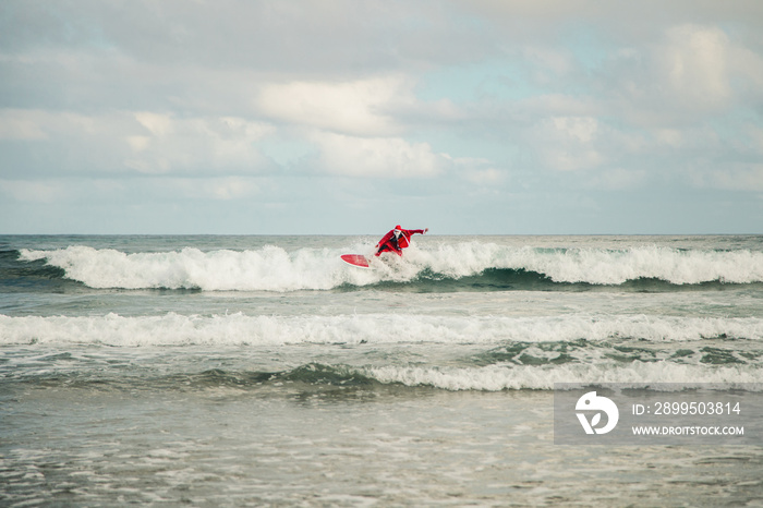 Young man surfer dressed as Santa Claus on the beach