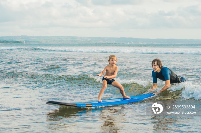 Father or instructor teaching his 4 year old son how to surf in the sea on vacation or holiday. Travel and sports with children concept. Surfing lesson for kids