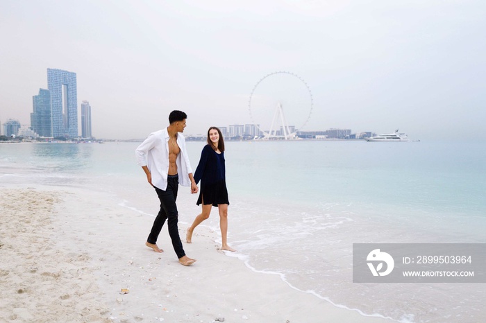 Young interracial couple walking on the beach holding hands