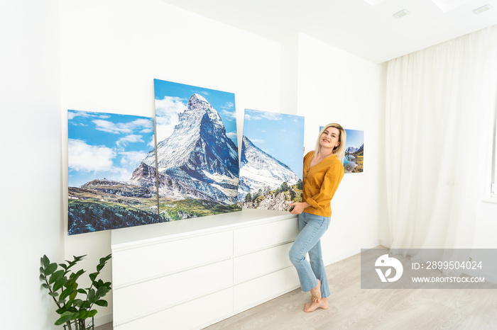 Canvas print with gallery wrap. Woman hangs photography on white wall. Hands holding photo canvas print