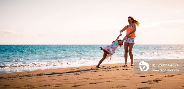 Happy mother and daughter having fun on tropical beach at sunset - Family playing next see during summer vacation - Concept of parent, love and happiness