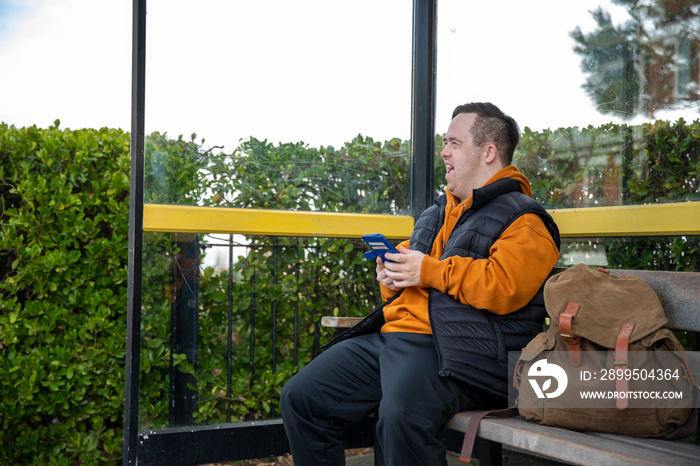 Man sitting on bench at bus stop, using smart phone