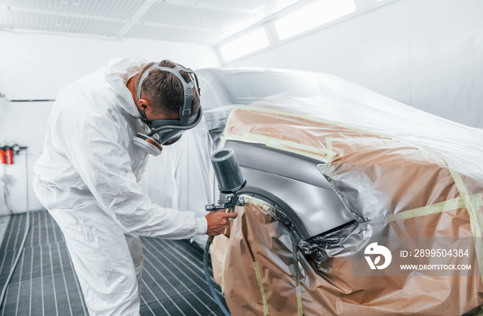 Painting job in progress. Caucasian automobile repairman in uniform works in garage