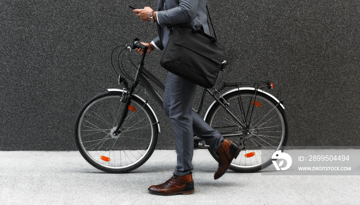 Businessman going to work with his bicycle and looking at phone.