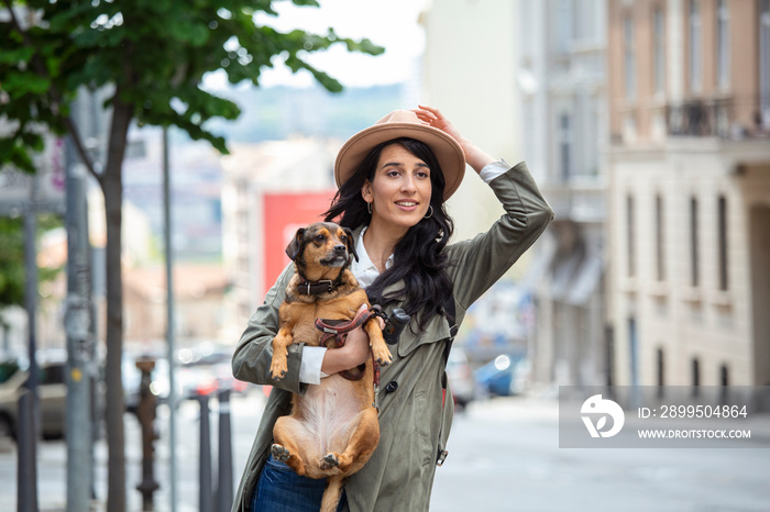 Young woman with dog waving to stop a taxi on the street. young female with funny dog stretching out arm and catching taxi while standing on roadside in city