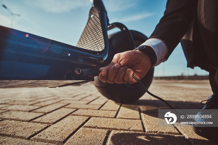 Elegant man is charging his electrical scooter with charger on special parking.