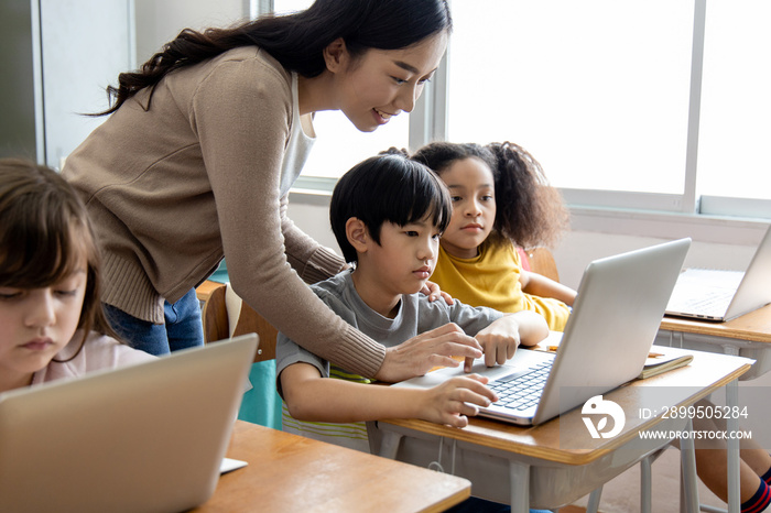 An Asian female teacher teaches primary school students to use computers and tablets to search for knowledge and information through the Internet. Classroom diversity students. Back to school concept