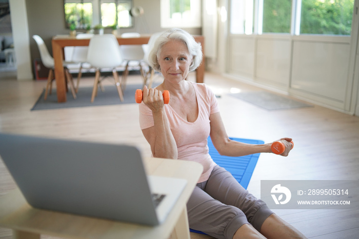 Senior woman doing fitness exercises at home through virtual class